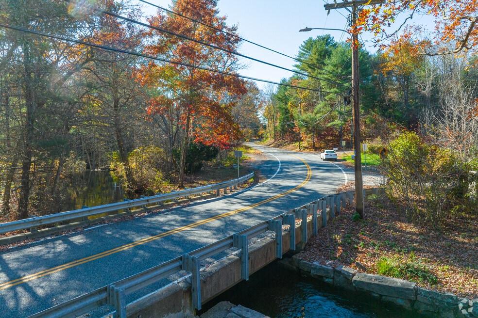 Curving road crosses a bridge over water beneath colorful autumn trees.