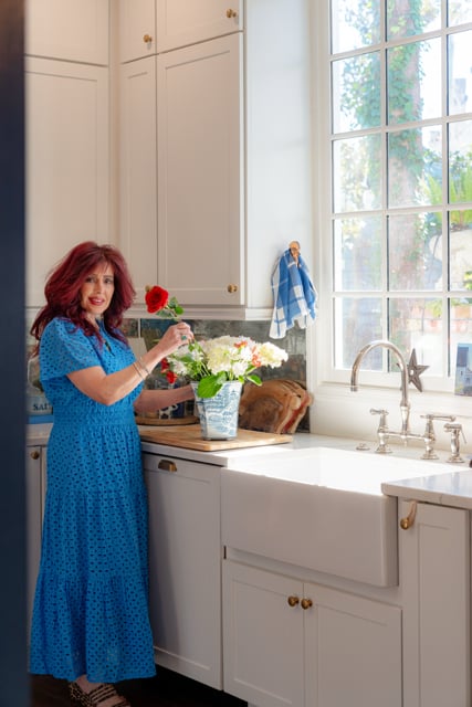 Real estate agent in a blue dress arranging flowers in a bright kitchen.