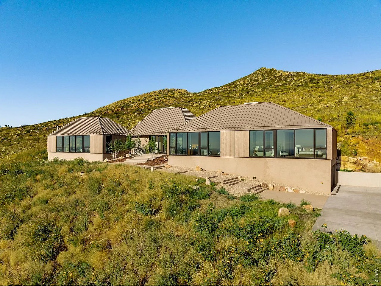 Modern angular home with broad windows and metal roofs on a rocky hillside beneath a mountain ridge.