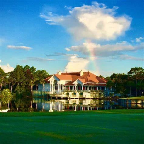 Waterfront building with a red tile roof reflected in a pond beneath a rainbow.