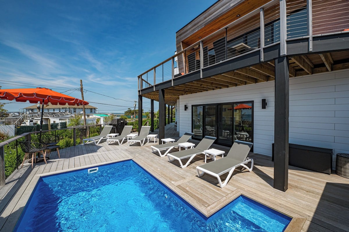 Modern coastal home beside an angular pool, with a raised deck and white loungers.