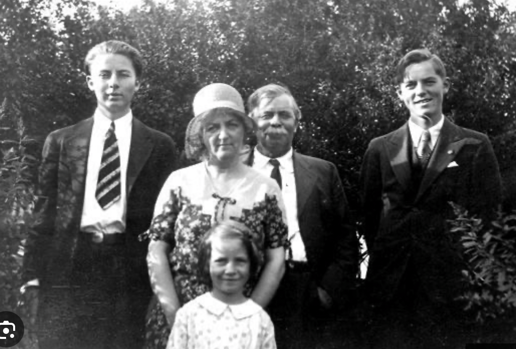 Five people pose outdoors in a vintage black-and-white family portrait, including a young girl in front.