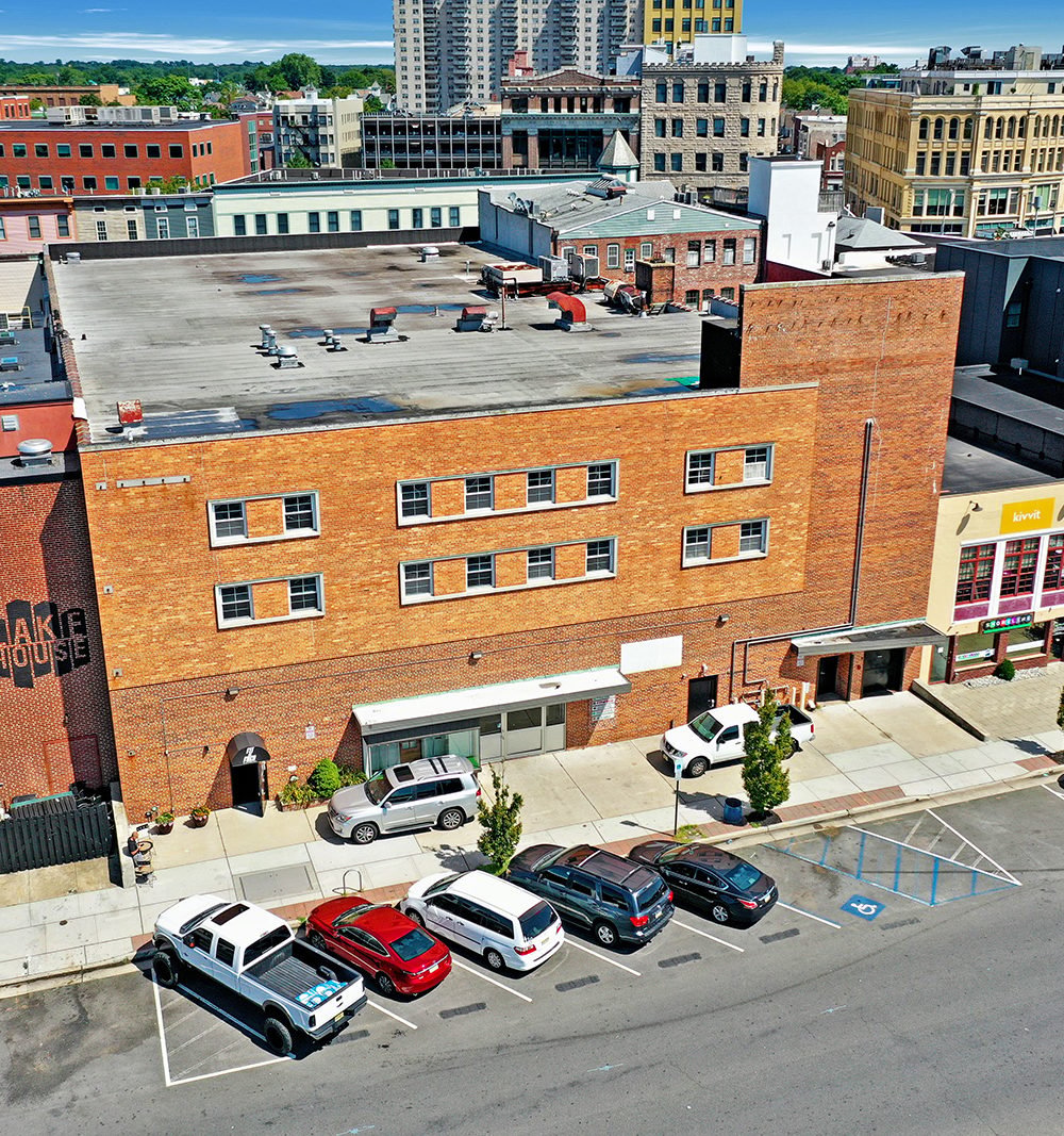 614 Cookman Avenue’s orange-red brick commercial building, viewed from above with parked cars along the street.