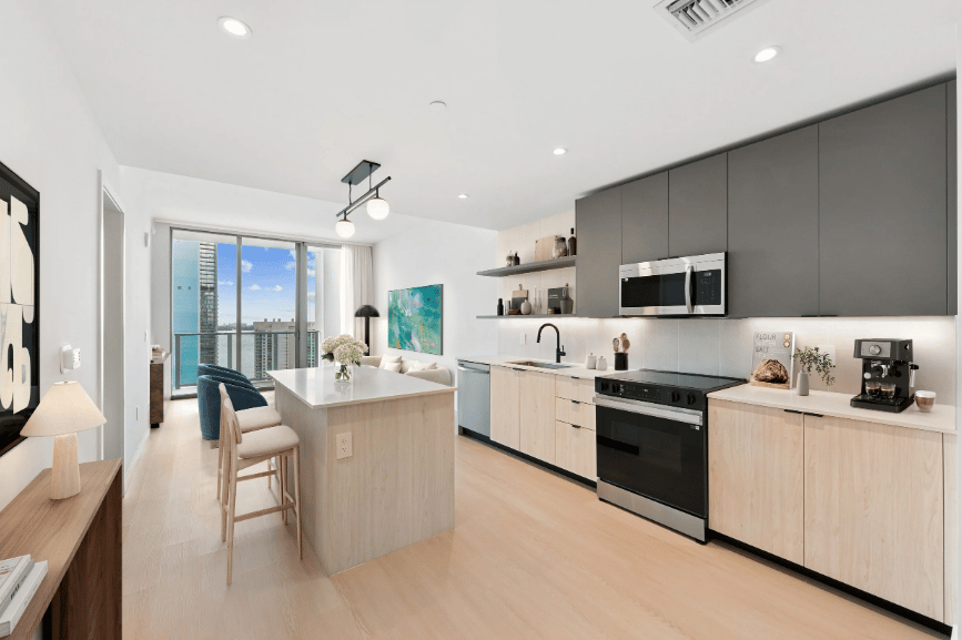 Modern apartment kitchen with a pale wood island and city views through sliding glass doors.