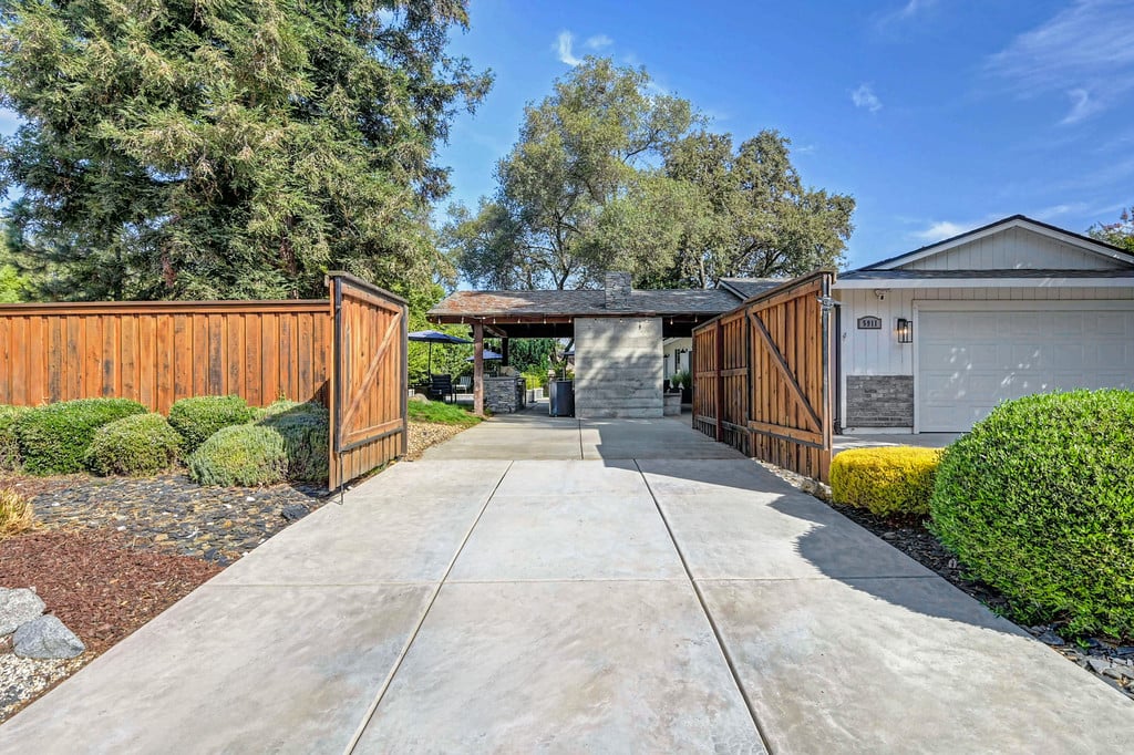 Home entrance with open wooden gates, a wide concrete driveway, and the garage.