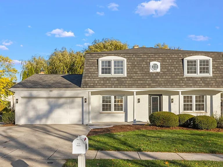 White two-story home with dark dormer roof, double garage, and covered entry.