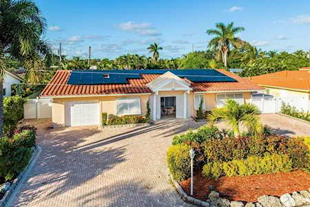 Single-story home with solar panels, a wide driveway, and tropical landscaping.