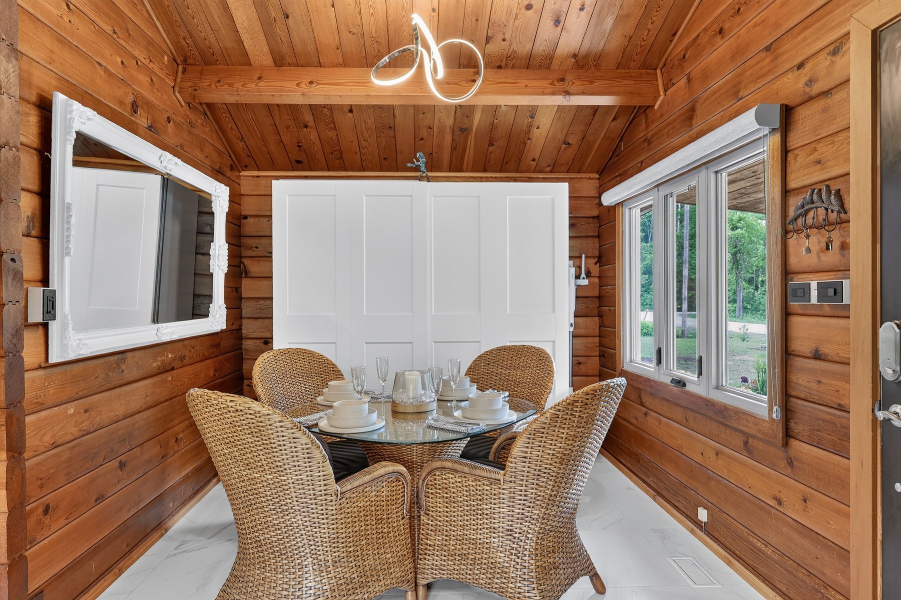 Dining area with wood-paneled walls, wicker chairs, and large windows overlooking a green yard.
