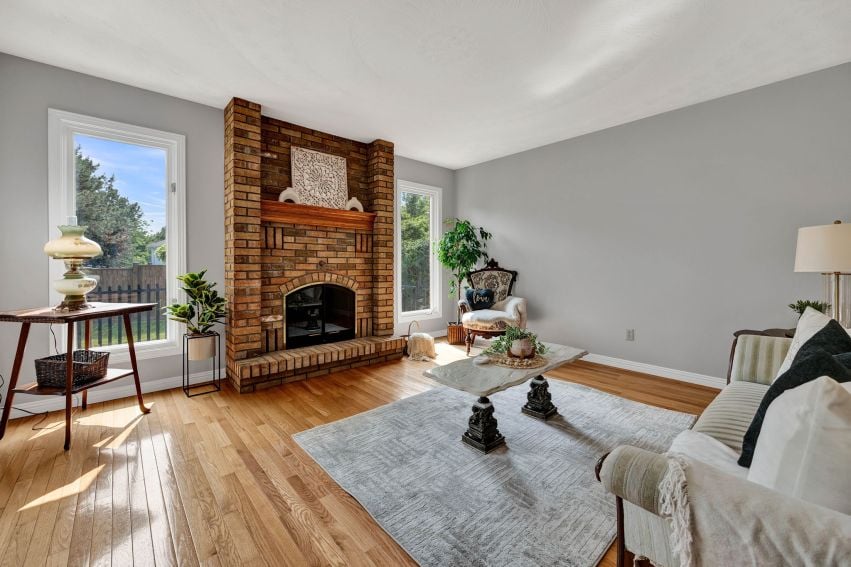 Living room with a large brick fireplace, hardwood floors, and tall windows.