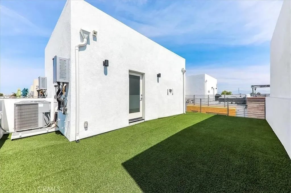  A bright rooftop patio with artificial turf, a white building, and a door leading to the inside.