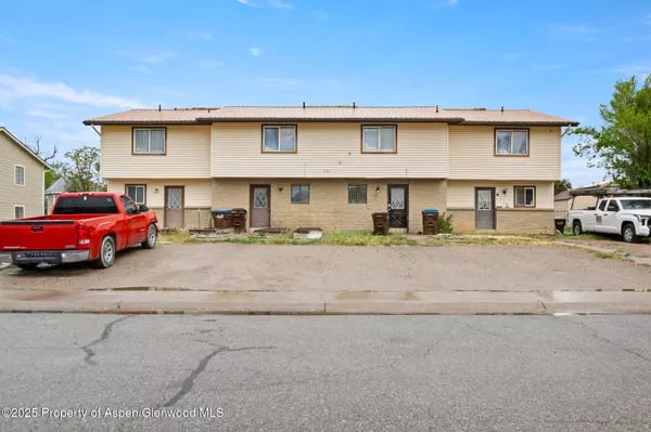 Beige two-story multi-unit building with red and white pickups parked in front.