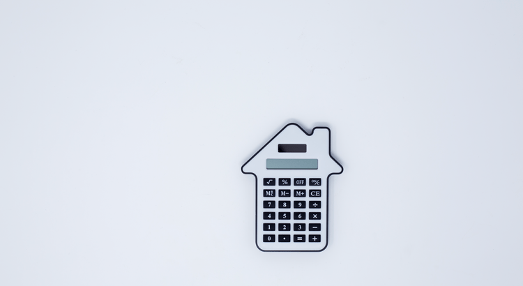 House-shaped calculator on a white background. The calculator has a small display screen above black buttons. The design emphasizes home budgeting.