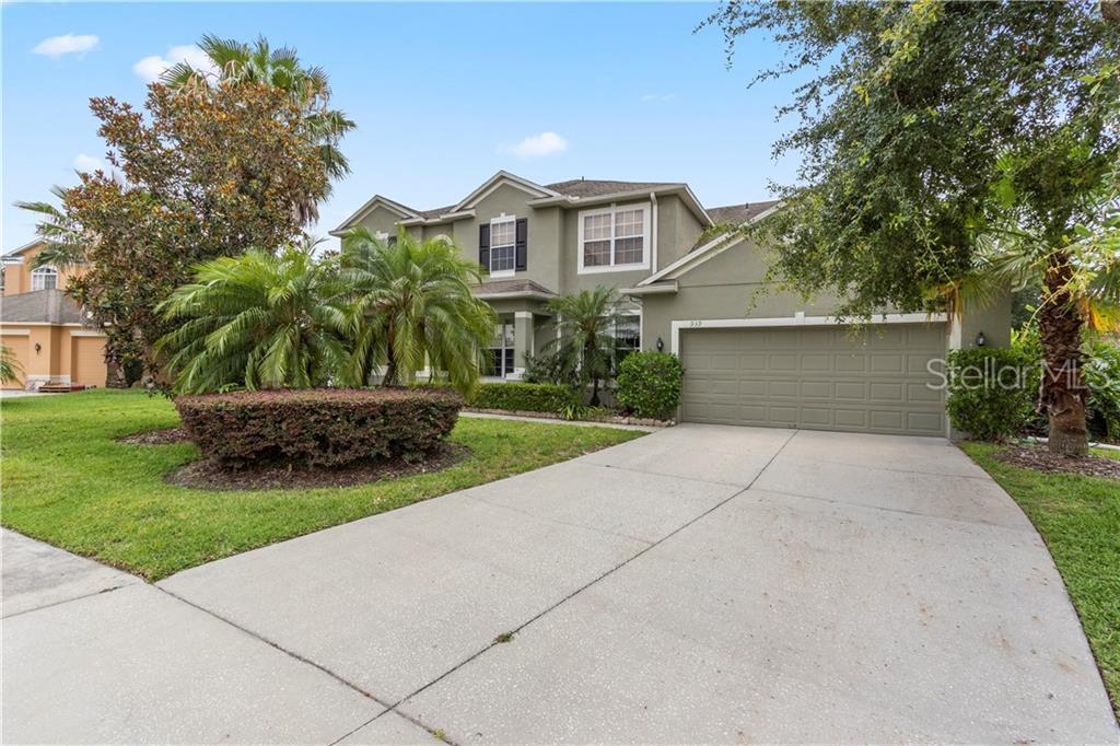 Two-story home with a wide driveway, palm trees, and a landscaped front lawn.