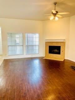 Empty living room with dark wood floors, two windows, and a corner stone fireplace.