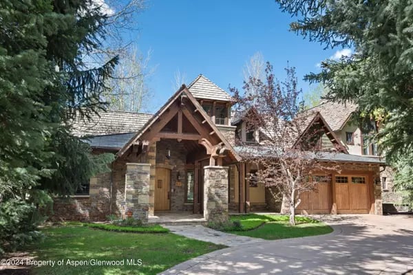 Mountain-style home with stone columns, timber gables, and a wooden garage door.