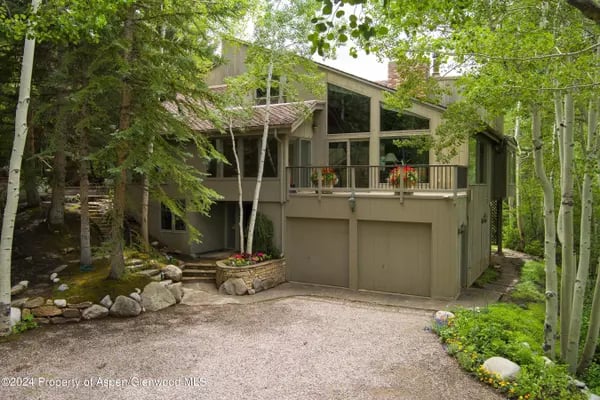 Aspen home with a raised balcony and attached garage, surrounded by leafy trees.