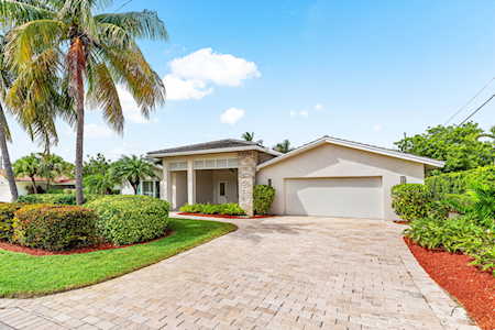 Single-story home with an attached garage, wide driveway, and palm trees.