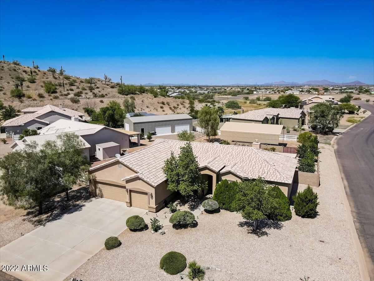 Aerial view of a tan stucco home with desert landscaping, neighboring homes, and distant mountains.