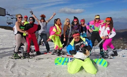 A group of skiers and snowboarders pose together on a snowy mountain slope.