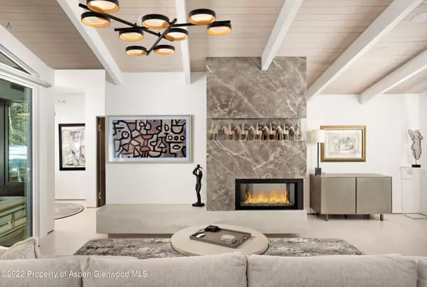 Contemporary living room with a marble fireplace, sculptural chandelier, and vaulted white beam ceiling.