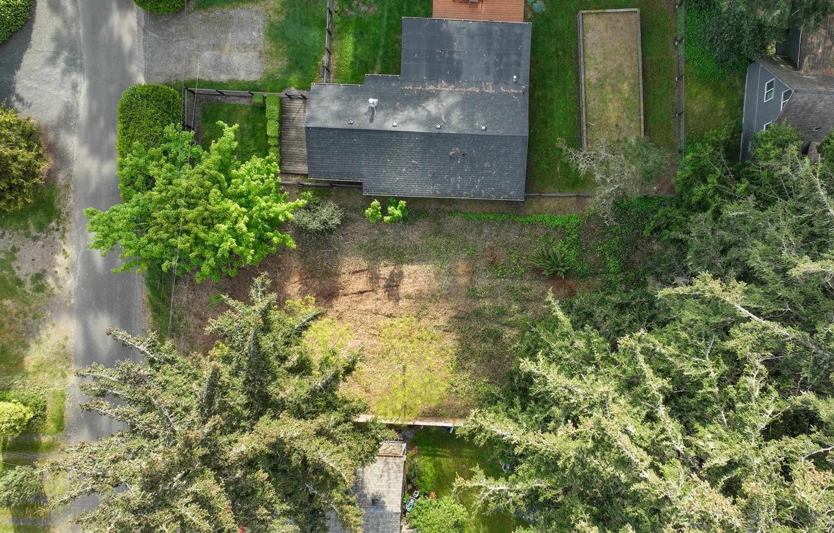 Aerial view of a wooded lot with a large clearing and a house near the rear edge.
