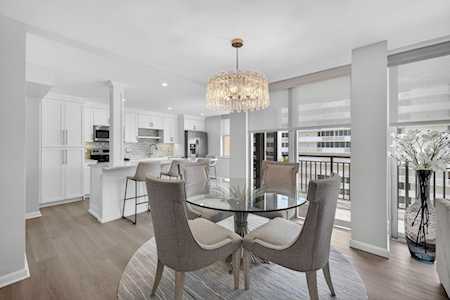 Open-plan dining area with a glass table, upholstered chairs, and a crystal chandelier beside the kitchen.