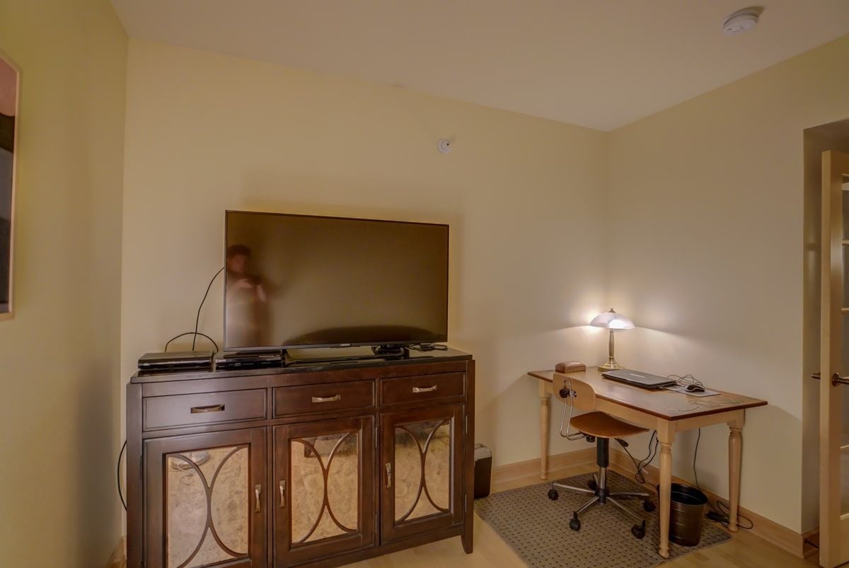 Furnished office with a wooden desk, rolling chair, and television on a decorative cabinet.