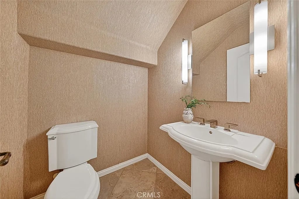 Powder room with a white pedestal sink, toilet, mirror, and tan textured walls.
