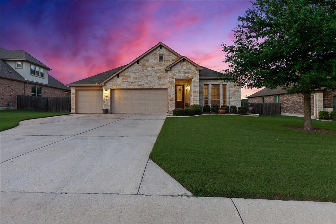 Stone-front home with a two-car garage and broad driveway beneath a pink dusk sky.