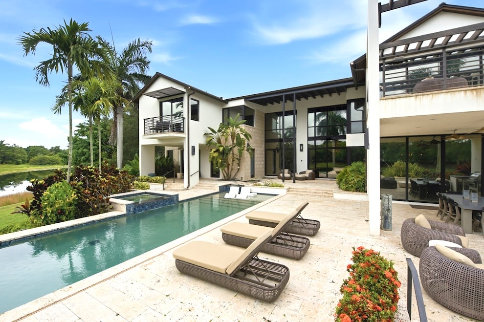 Contemporary home with a pool, spa, stone patio, and palm-lined waterway view.