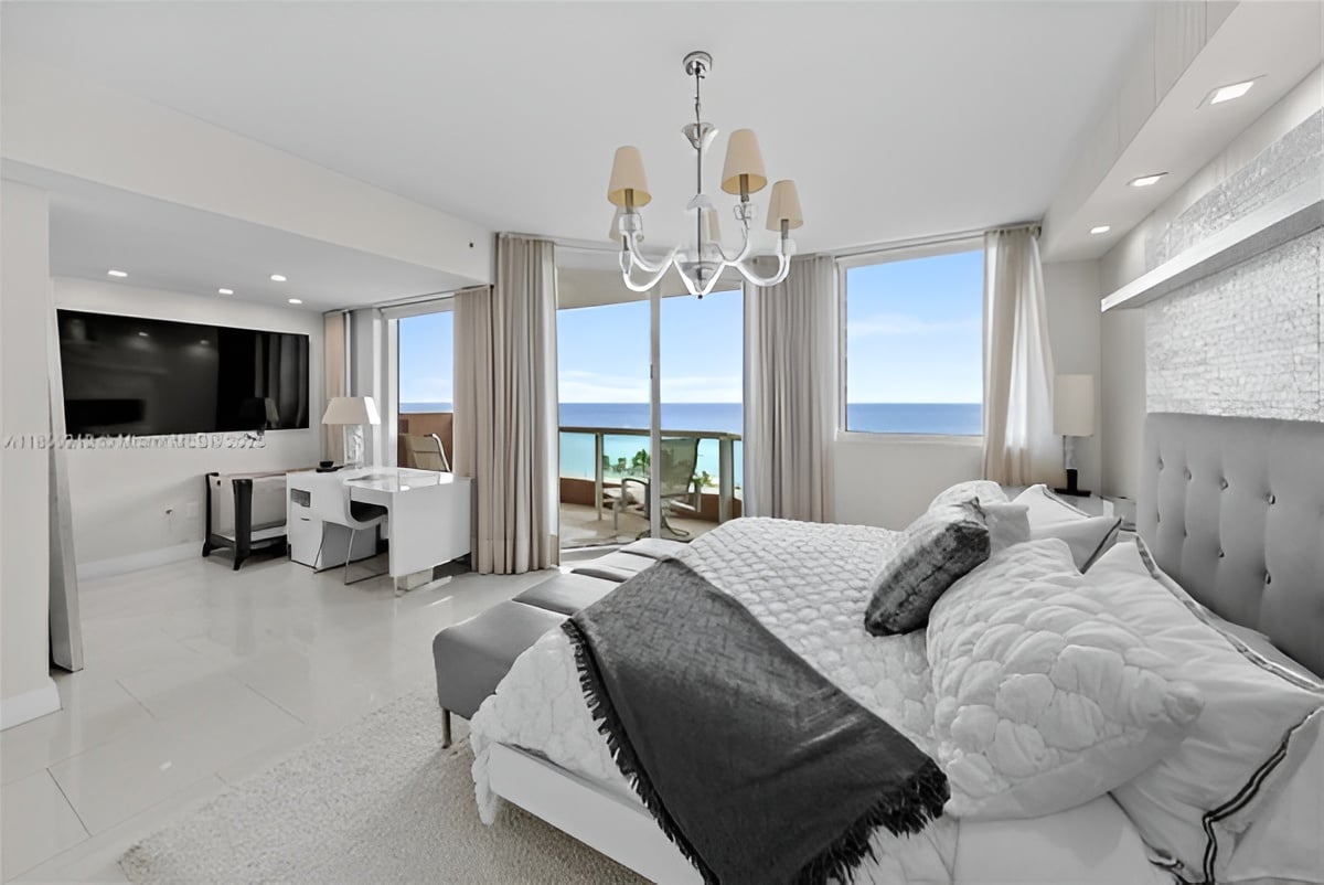 Furnished bedroom with a king bed and floor-to-ceiling windows overlooking the ocean.