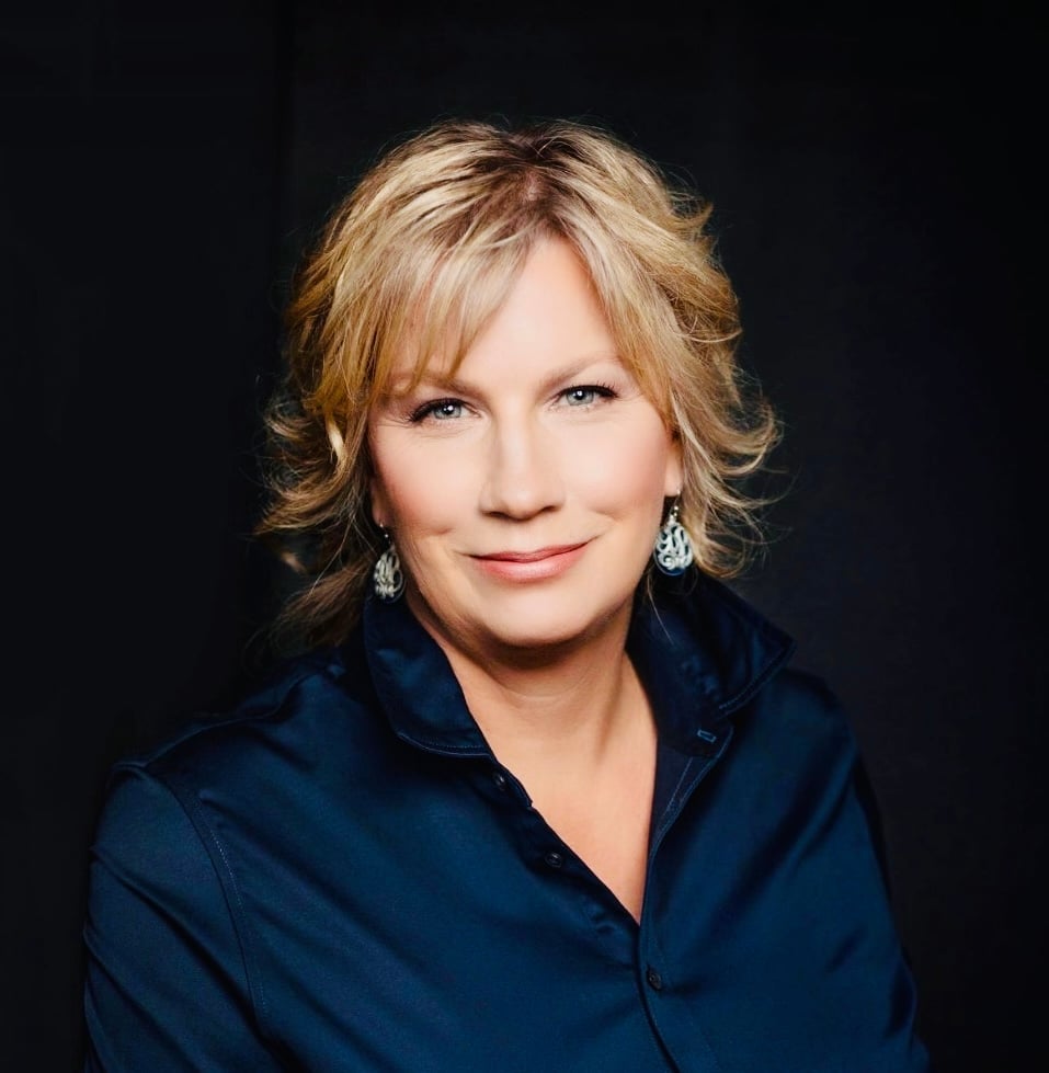Jodi Gaines wearing a dark blue collared shirt and dangling earrings.
