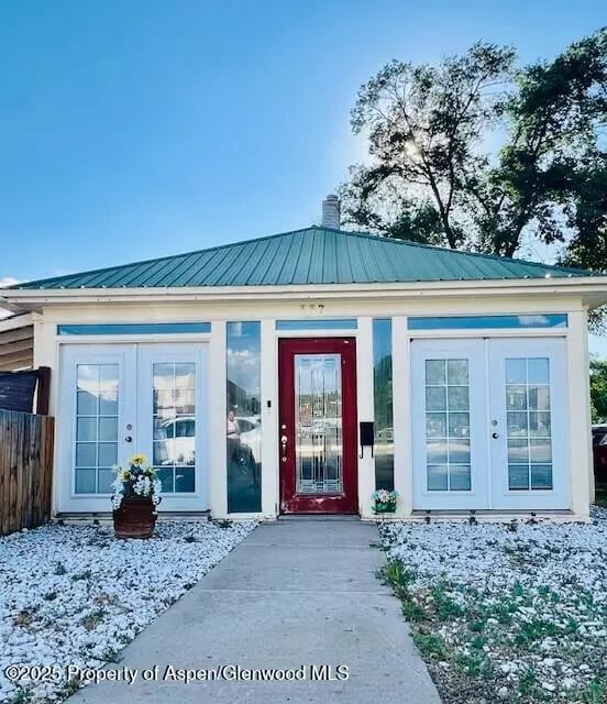 White home with a teal metal roof, red front door, and glass-paneled doors flanking the entrance.