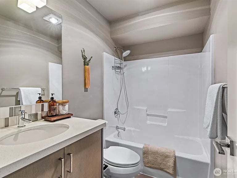 Bathroom with a white tub and shower beside a wood-front vanity.
