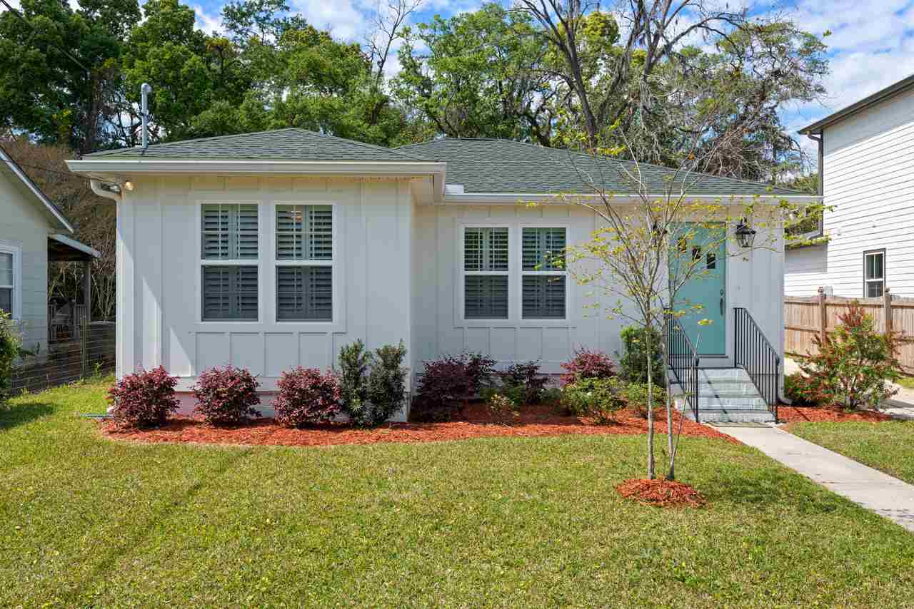 A small white house surrounded by lush green grass and vibrant shrubs.