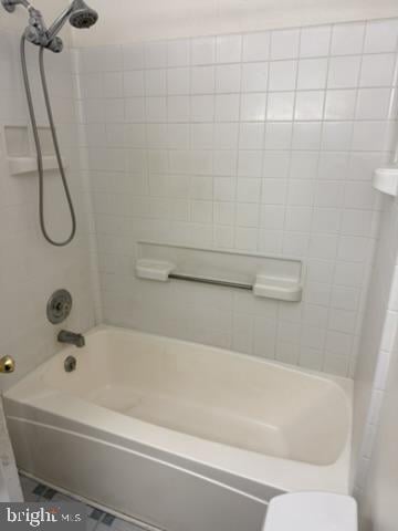 White bathtub and tiled shower with a handheld showerhead and grab bar.