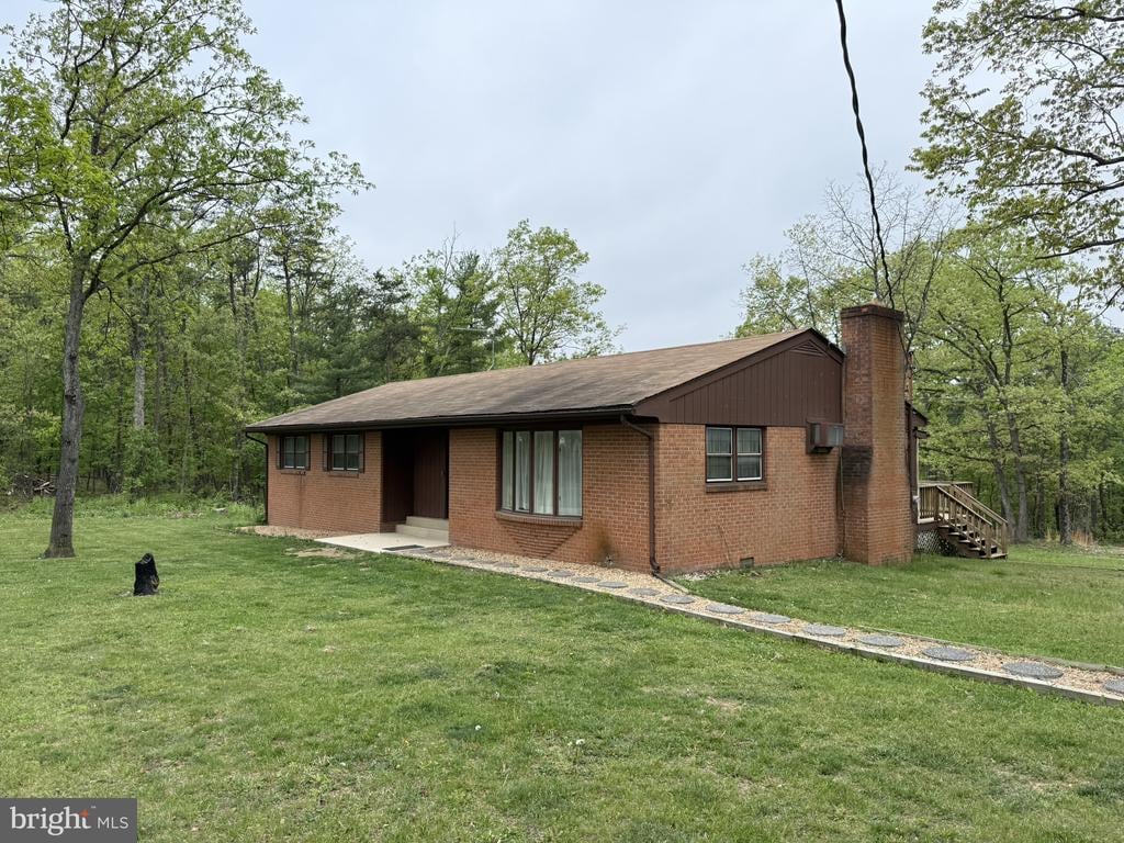 One-story brick house with a tall chimney, broad lawn, and wooded surroundings.