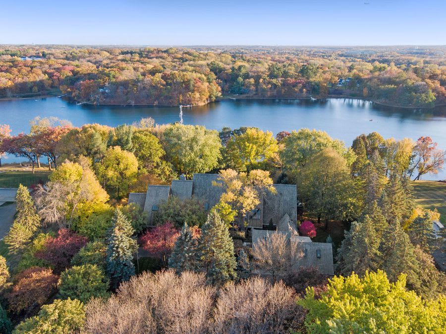  Aerial view of a house surrounded by trees and a lake in the fall.