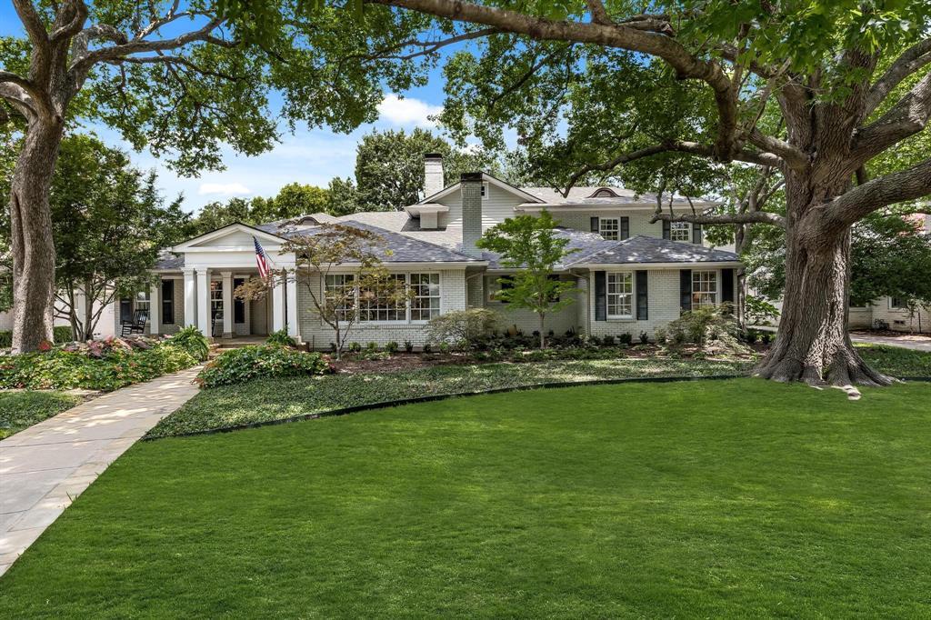 Light brick home with a covered entry and American flag, framed by mature trees and a broad lawn.