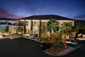 Modern low-rise building beside a parking lot, with landscaped grounds and mountains at dusk.