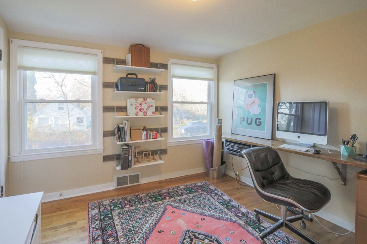 Home office with open shelves, an iMac desk, black leather chair, and colorful patterned rug.