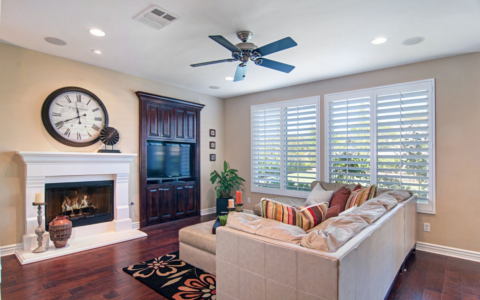 Living room with a white fireplace, dark built-in cabinet, and large plantation-shuttered windows.