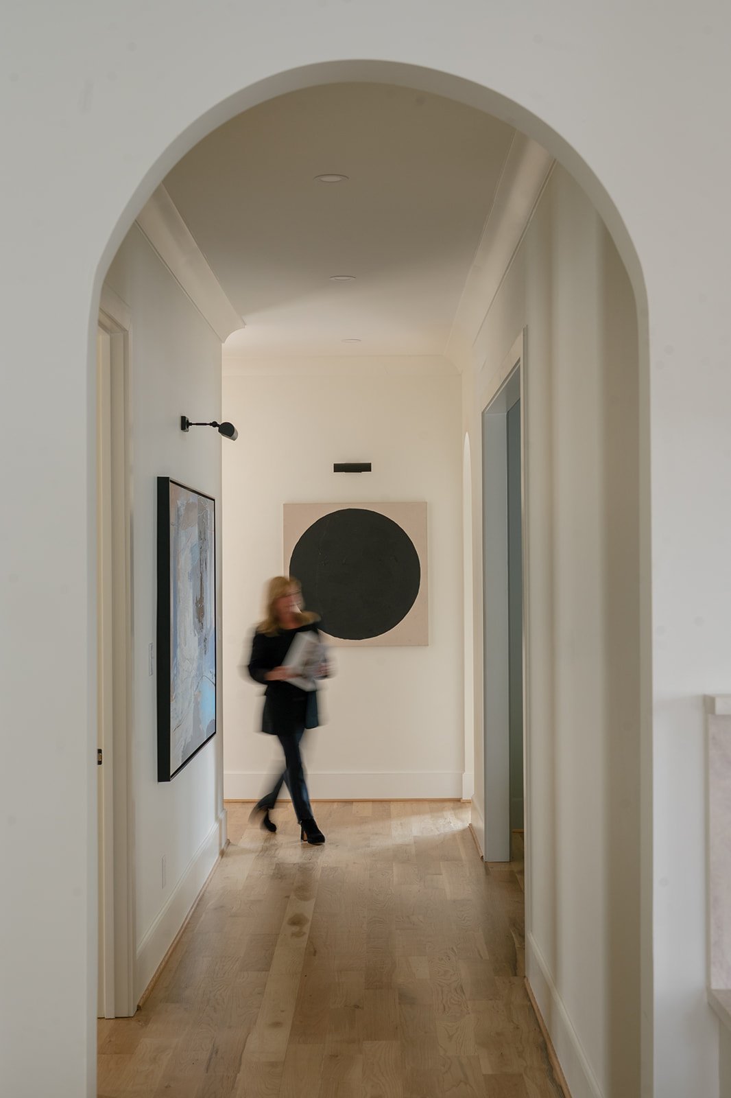 Bright home hallway with light wood floors, an arched entrance, and abstract artwork.