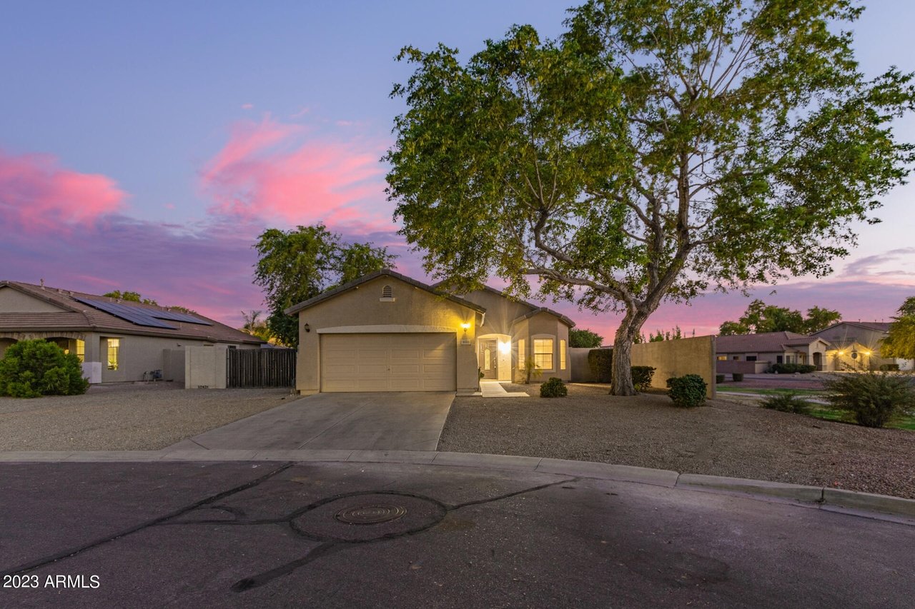 Single-story home with a two-car garage and large shade tree at dusk.