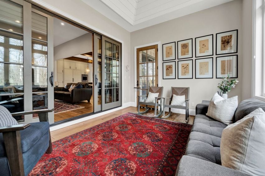 Living room with vaulted ceiling, glass doors, gray sofas, rocking chairs, and a red patterned rug.
