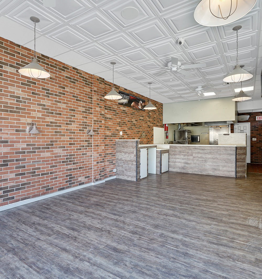 Vacant commercial space with a service counter, brick walls, and pendant lighting.