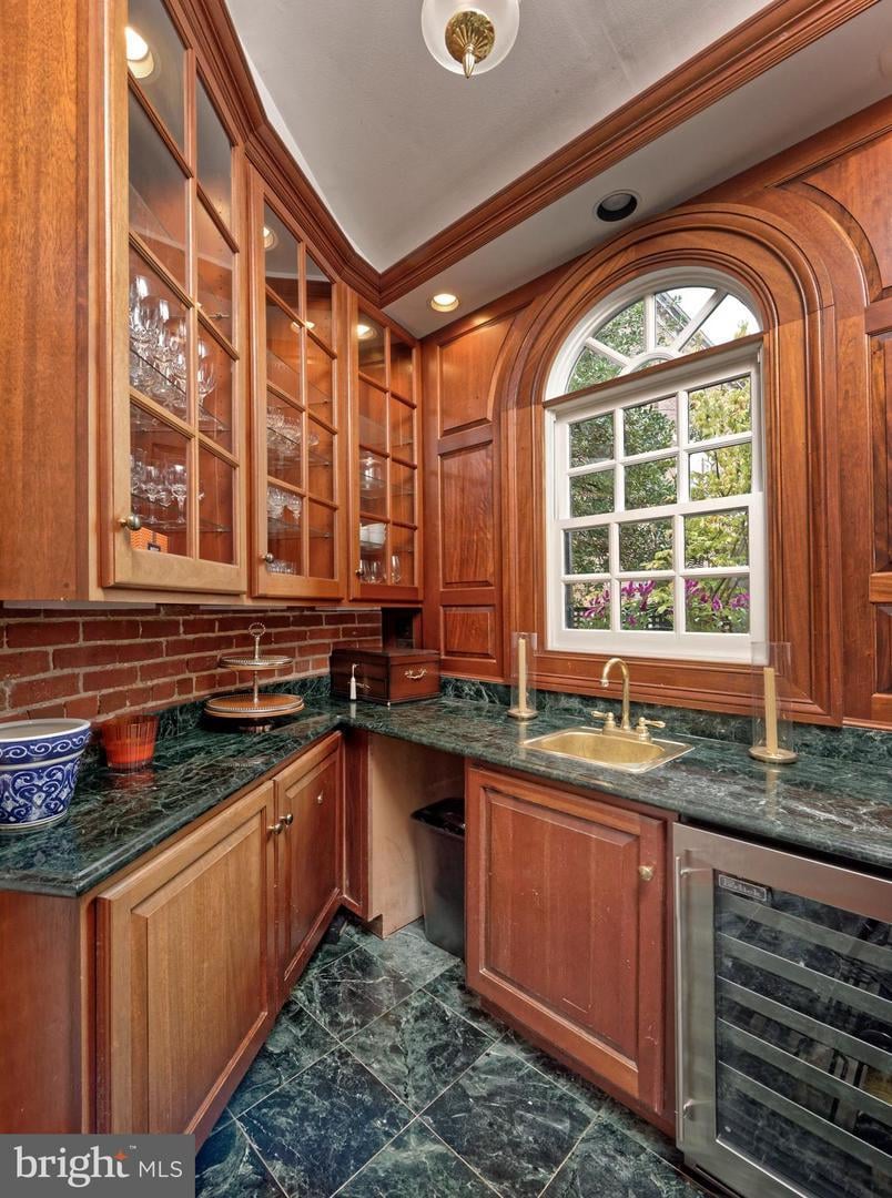 Kitchen with cherry-toned cabinetry, green marble counters, and a brass sink beneath an arched window.