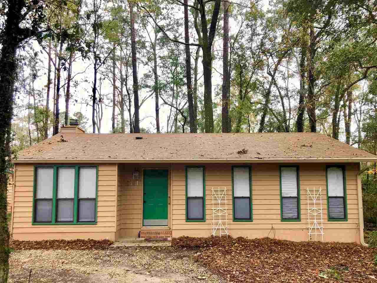 A quaint house with green shutters nestled among lush trees in a serene woodland setting.