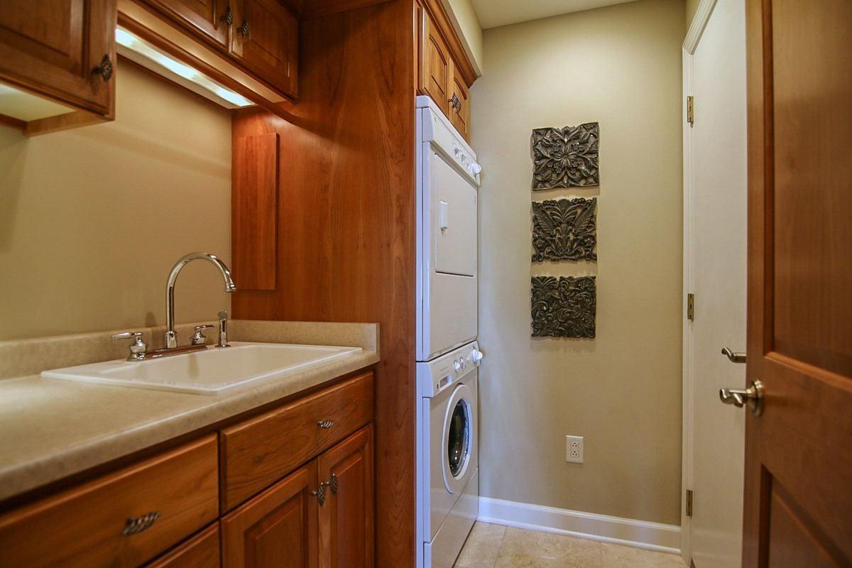 Laundry room with stacked washer and dryer, a built-in sink, and wood cabinetry.