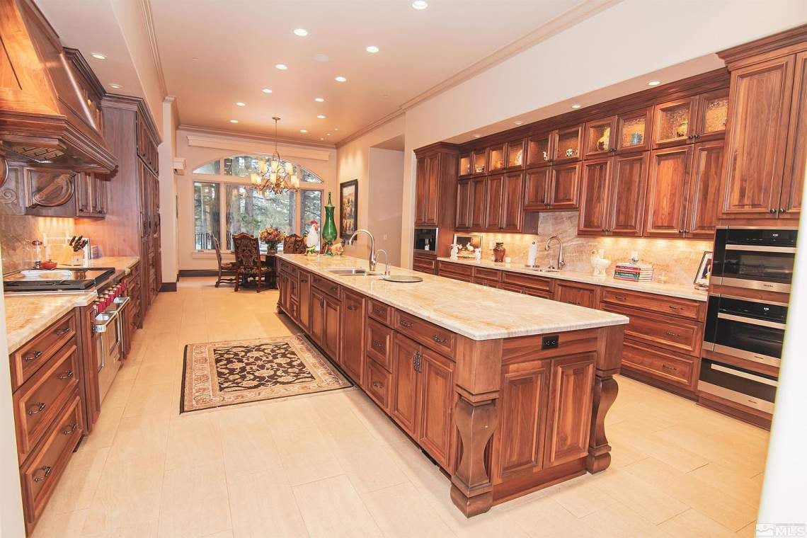 Luxury kitchen with dark wood cabinets, a large stone island, and an arched window by the dining area.